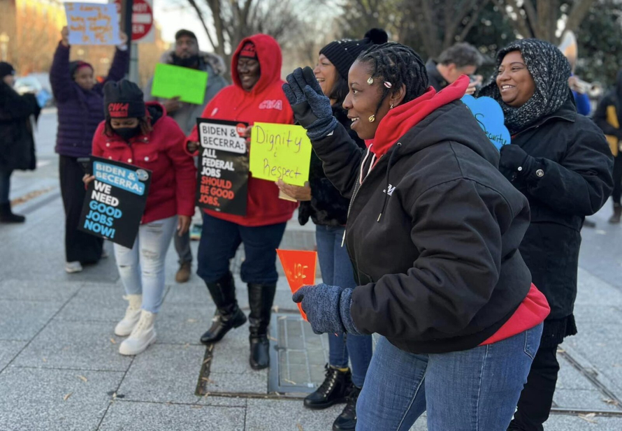 A group of 6 Black women in a circle holding picket signs and wearing coats.