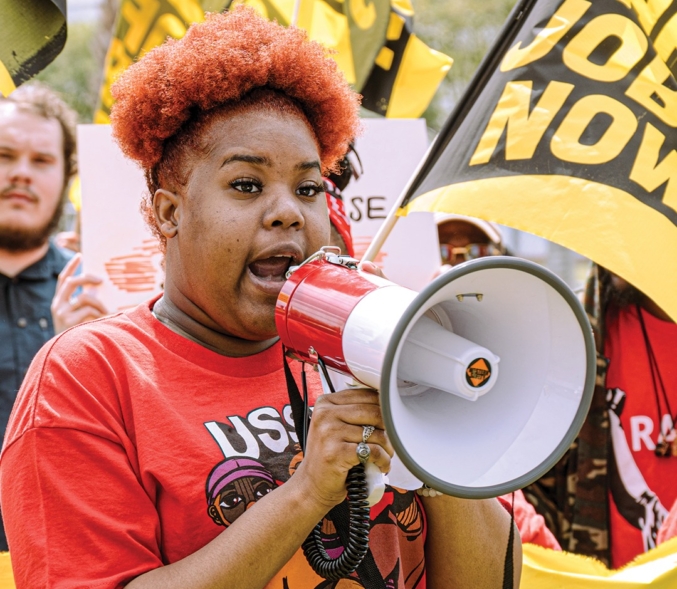 A picture of worker Naomi Harris, speaking with a bullhorn at an action.