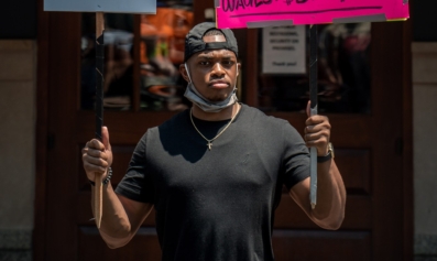 A Black restaurant worker at an action holds two signs. One says, 
