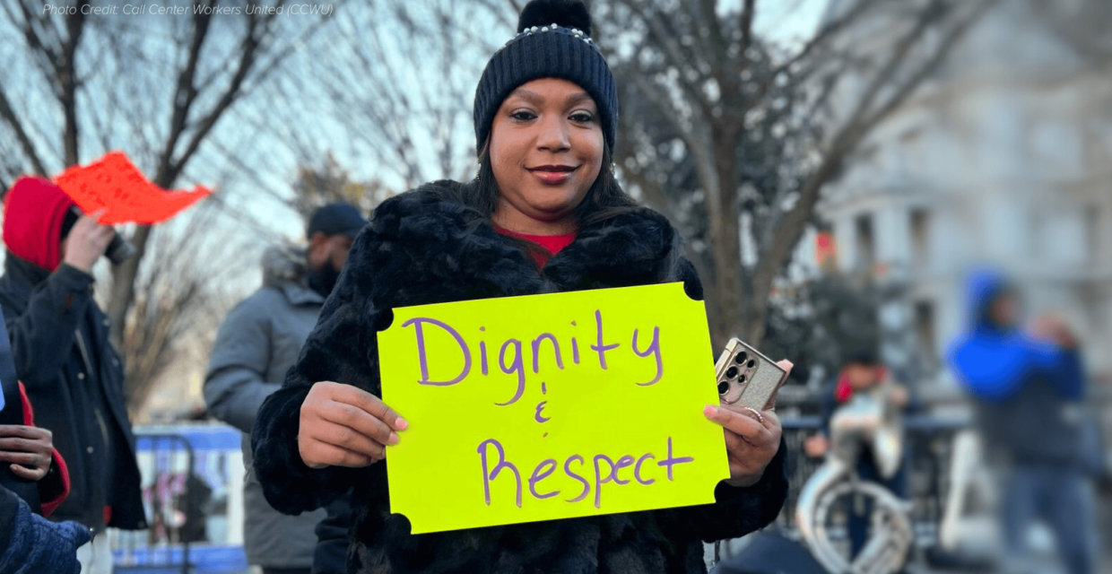 Black woman in black knit cap and coat standing outside in a protest holding a bright yellow handwritten sign that reads Dignity and Respect.