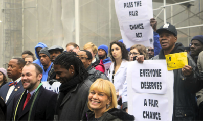 A crowd of people at an action. One man holds a sign that reads "Everyone deserves a fair chance."