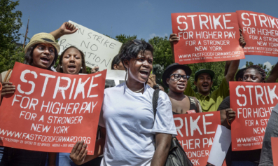 Fast food workers at a rally. Their signs read "Strike for Higher Pay."