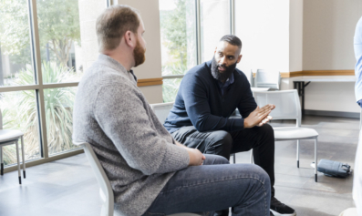 Two men sit in a semi-circle, speaking to one another.