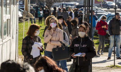 Unemployed workers stand in a line on a sunny day.