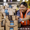 A Black woman warehouse worker moves Amazon boxes on a conveyor belt