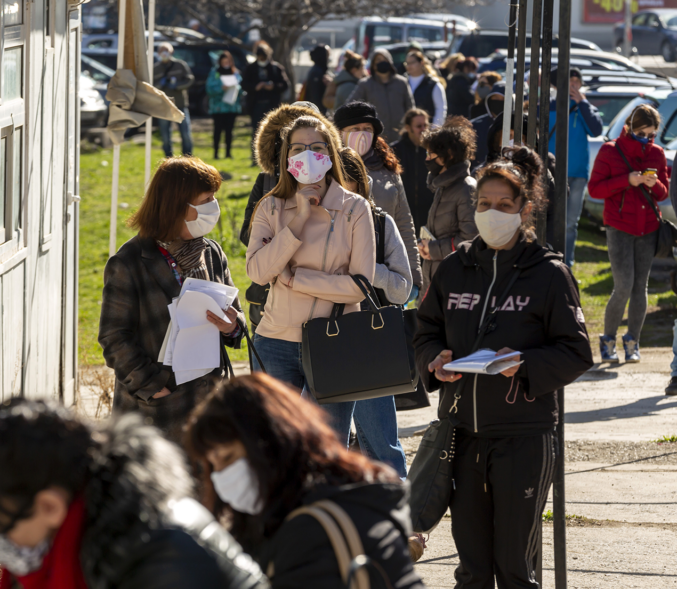 Unemployed workers stand in a line on a sunny day.