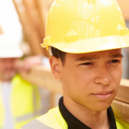 A young construction worker carries wooden beams with a coworker
