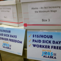 Banker boxes with sign reading "Alaska- An Act Increasing the Minimum Wage" and "$15/hour, paid sick days, worker freedom, Better Jobs for Alaska"