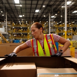 Amazon worker packs boxes in a large warehouse.