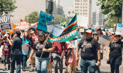 A multicultural march of May Day strike demonstrators carry a sign reading "Resiste!"