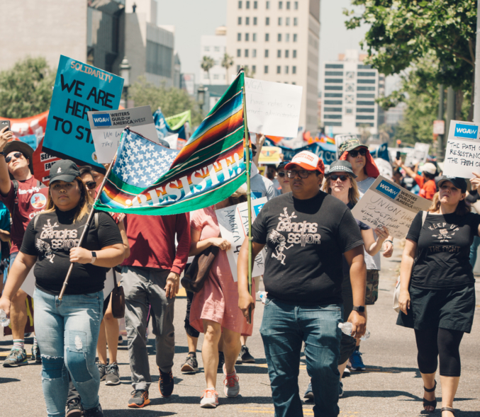 A multicultural march of May Day strike demonstrators carry a sign reading "Resiste!"