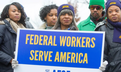 A group of Black government workers attend a rally. A woman wearing an AFGE cap holds a blue and yellow sign that reads, "Federal Workers Serve America". Photo source: American Federation of Government Employees (AFGE)