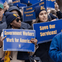 A group of AFGE marchers carry royal blue signs that reads, "Save Our Services," and "Government Workers Work for America". Federal Workers