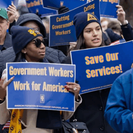 A group of AFGE marchers carry royal blue signs that reads, "Save Our Services," and "Government Workers Work for America". Federal Workers