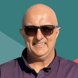 Image: Portrait of a bald man wearing glasses and a purple shirt, standing in front of a colorful geometric background.