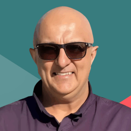 Image: Portrait of a bald man wearing glasses and a purple shirt, standing in front of a colorful geometric background.