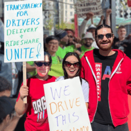 A trio of workers with Colorado Independent Drivers United wearing red, carry signs that say, 'Transparency for Drivers - Delivery and Rideshare Unite!', and 'We Drive This Economy'.