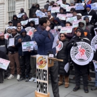 Crowd of app-based ridehail drivers and delivery workers protesting outside New York's City Hall, holding signs and banners reading "Driver Power", "We deserve job security", “End unfair deactivations” and union logos. They are calling for just cause protections.