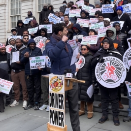 Crowd of app-based ridehail drivers and delivery workers protesting outside New York's City Hall, holding signs and banners reading "Driver Power", "We deserve job security", “End unfair deactivations” and union logos. They are calling for just cause protections.