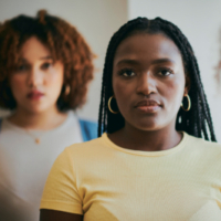 A portrait of a young Black women wearing a yellow shirt stands at the center of two other women.