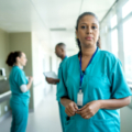 A Latine woman healthcare worker stands before colleagues in discussion.