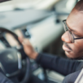 A Black man in a car looks out to his left-side mirror.